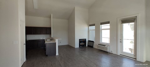 an empty living room with a kitchen in the background