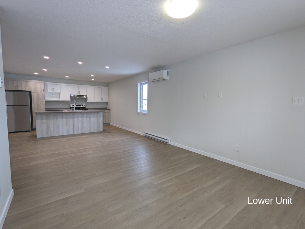 an empty living room and kitchen with wood flooring and white walls