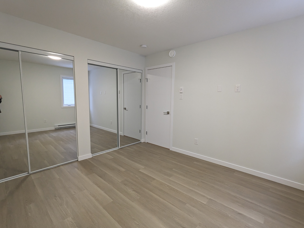 an empty living room with mirrors and wood flooring
