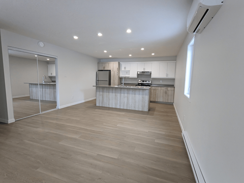 an empty living room with a kitchen and a large mirror