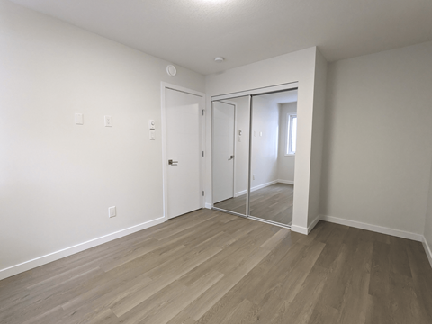 a bedroom with white walls and wood flooring and a mirrored closet