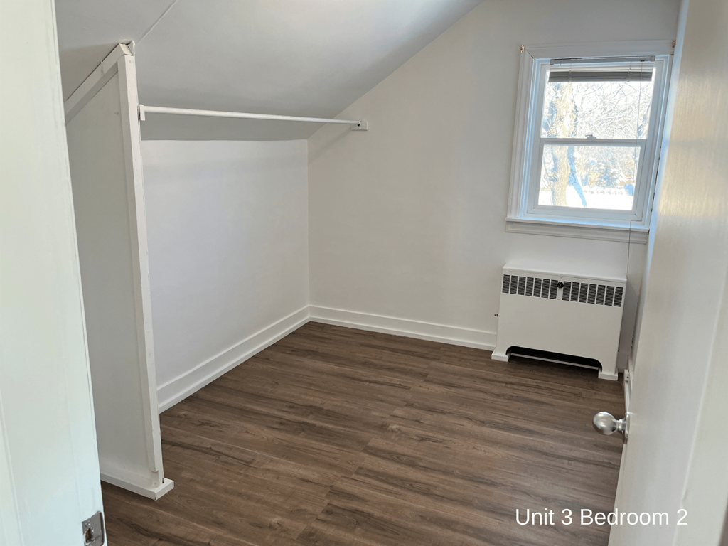 a small room with white walls and wood flooring and a window