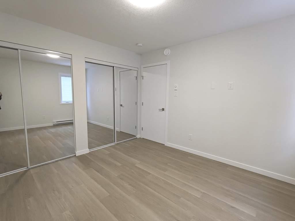 an empty living room with mirrors and wood flooring