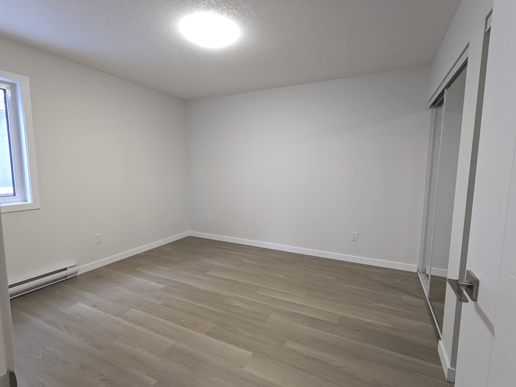 a bedroom with white walls and wood flooring and a window