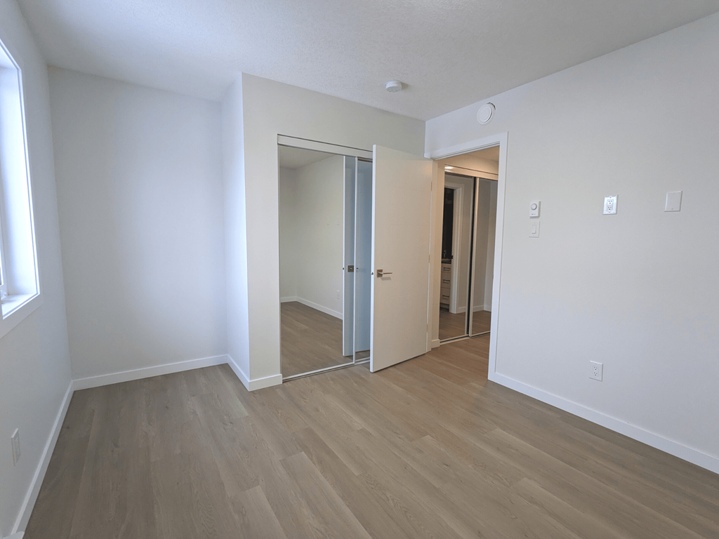 an empty living room with wood flooring and a mirrored closet