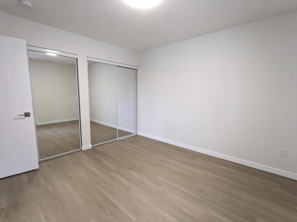 an empty bedroom with wood flooring and mirrored closet doors