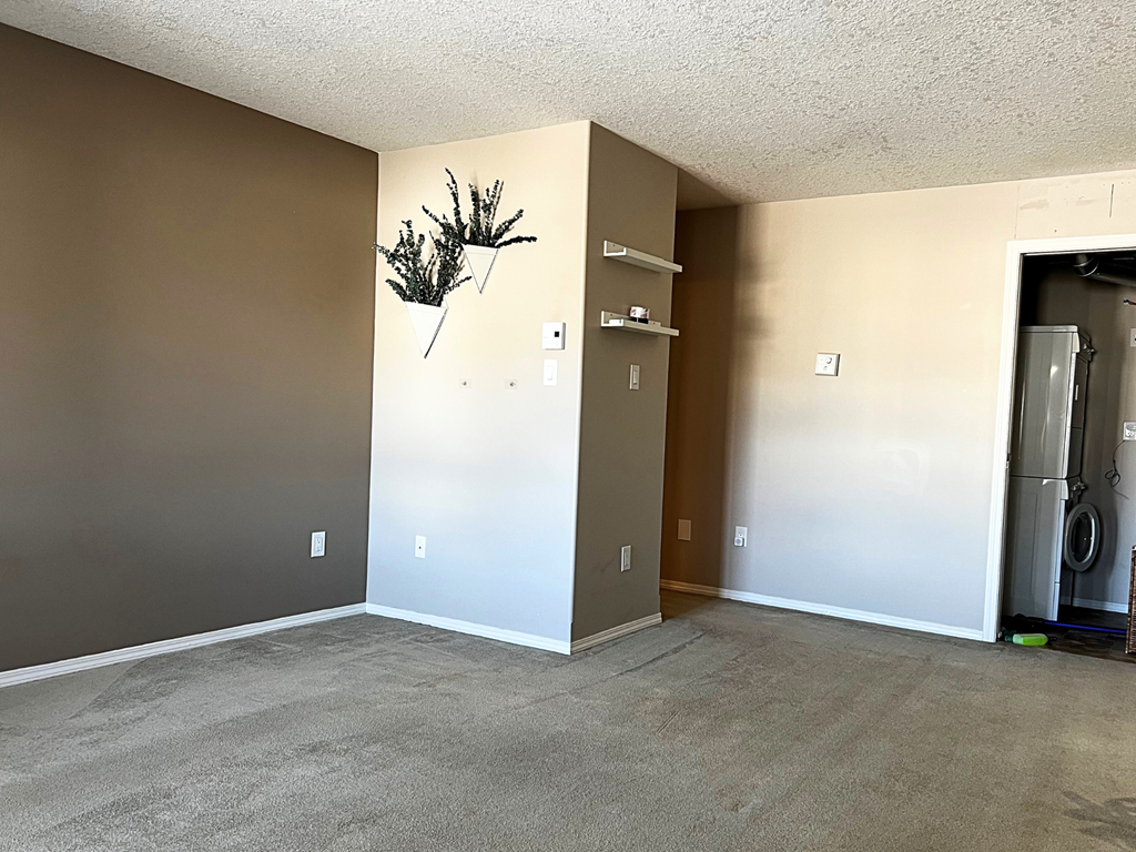 an empty living room with a refrigerator in the corner