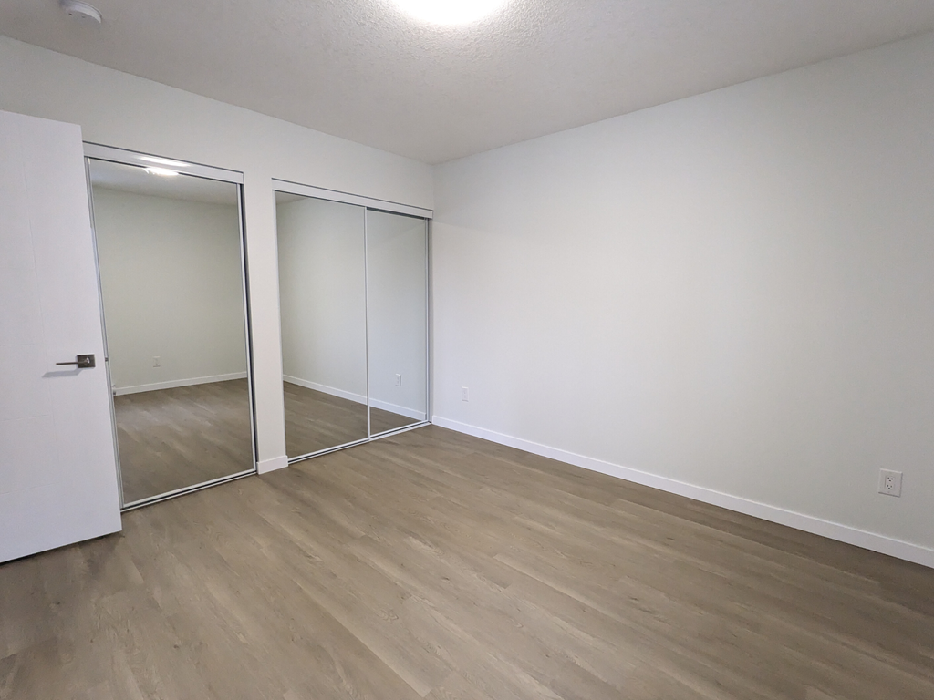 an empty bedroom with wood flooring and mirrored closet doors