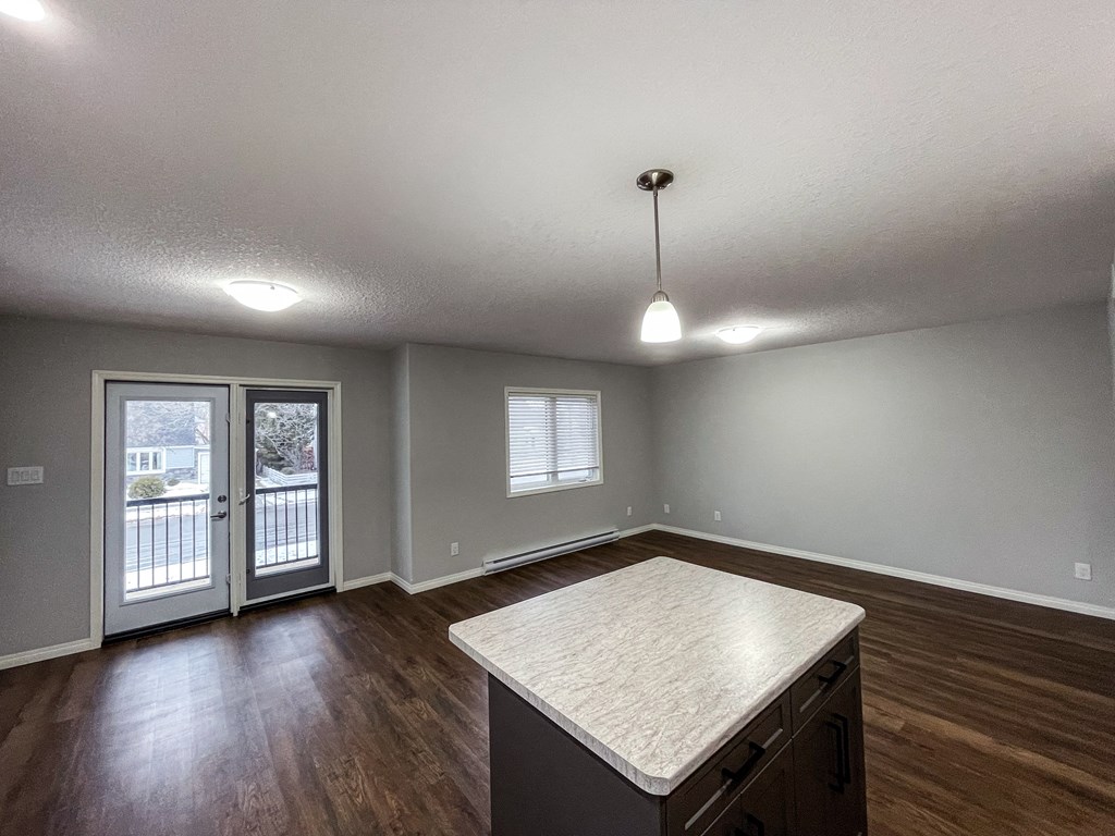 an empty living room with a kitchen island and a door to a balcony