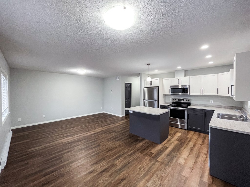 an empty kitchen and living room with wood floors and white cabinets