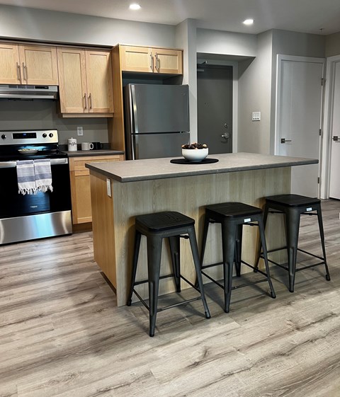 A kitchen with a black fridge and stove, wooden cabinets, and a bar area with three stools.