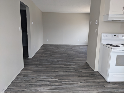 an empty kitchen with white appliances and a wood floor