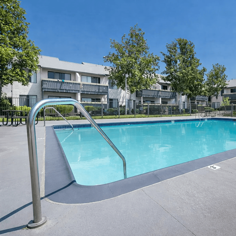A swimming pool with a ladder in the foreground and apartment buildings in the background.