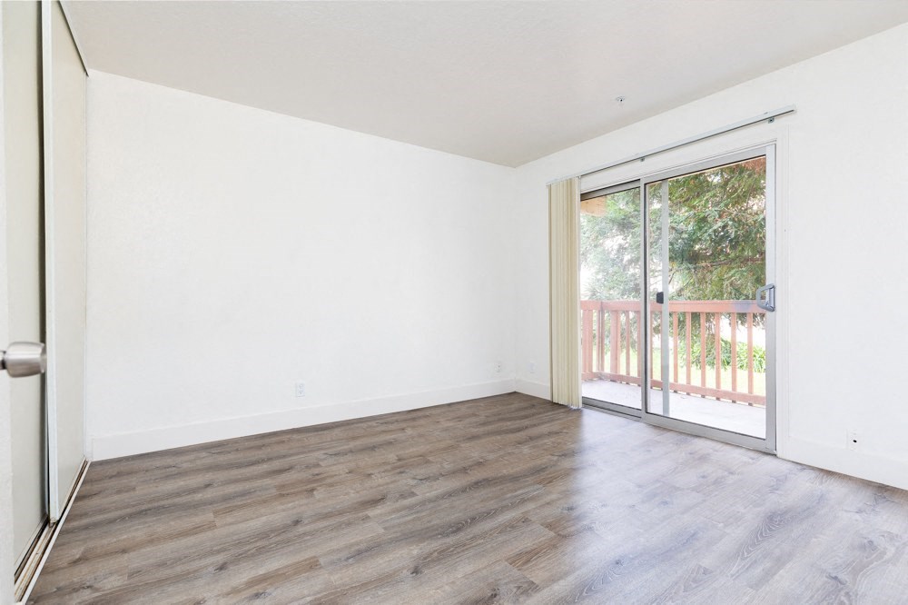an empty living room with a sliding glass door to a balcony