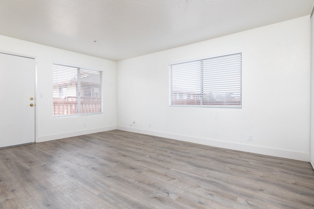 the living room of an apartment with white walls and wood flooring