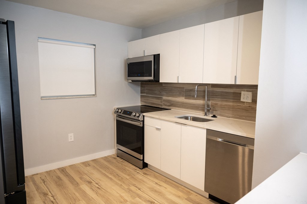 an empty kitchen with white cabinets and stainless steel appliances and a window
