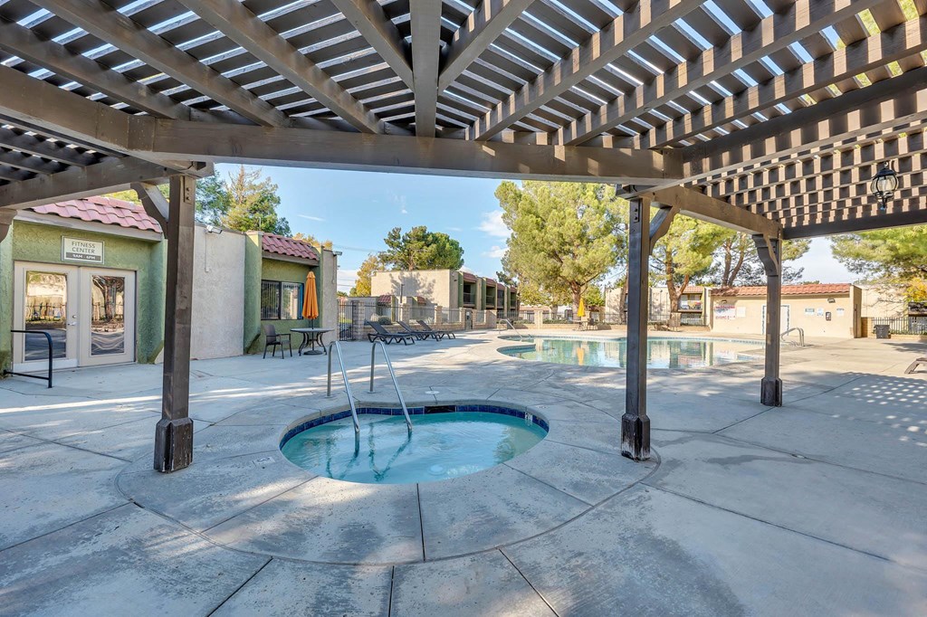 a hot tub is under a pergola on a patio next to a pool