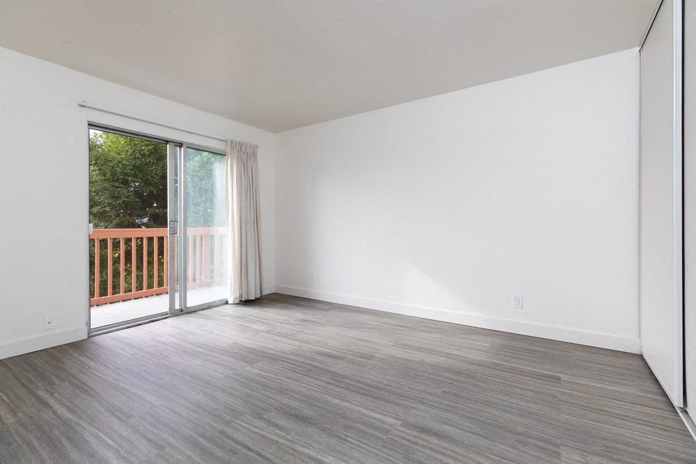 an empty living room with a sliding glass door to a balcony