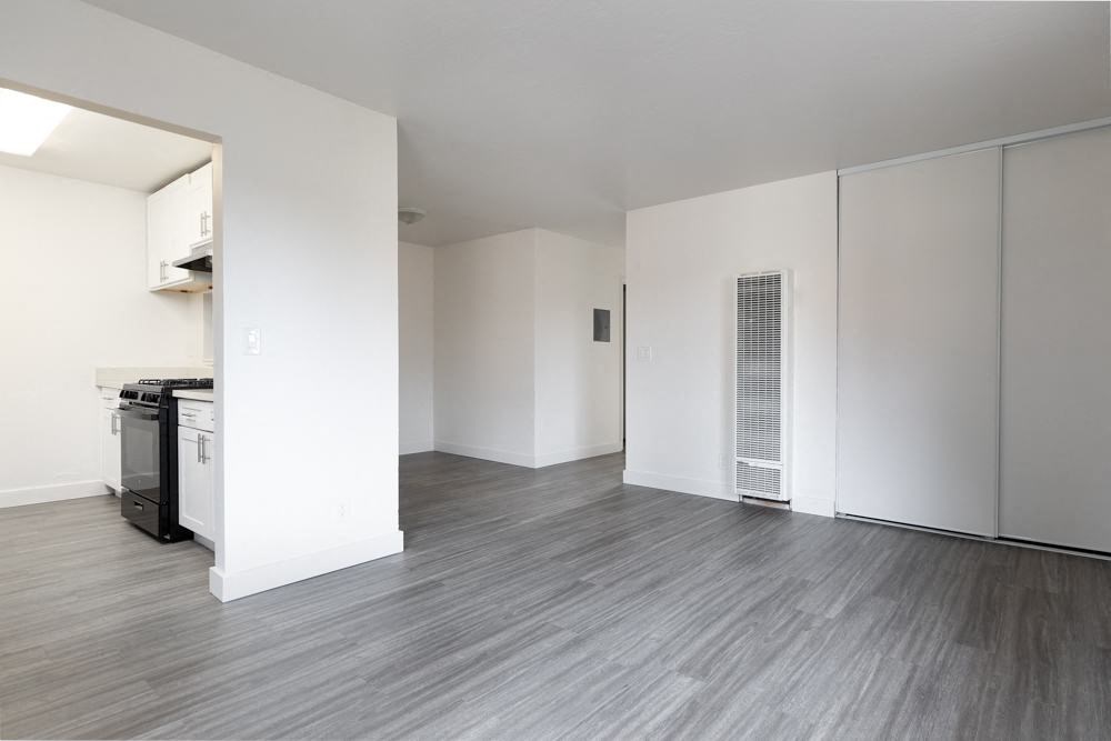 an empty living room and kitchen with white walls and wood floors