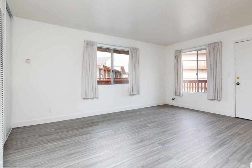 an empty living room with a door and two windows
