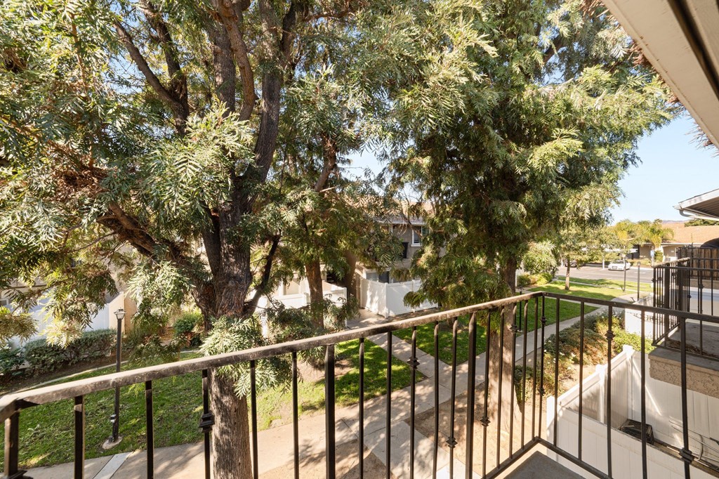 A balcony with a metal railing overlooks a tree and a house.