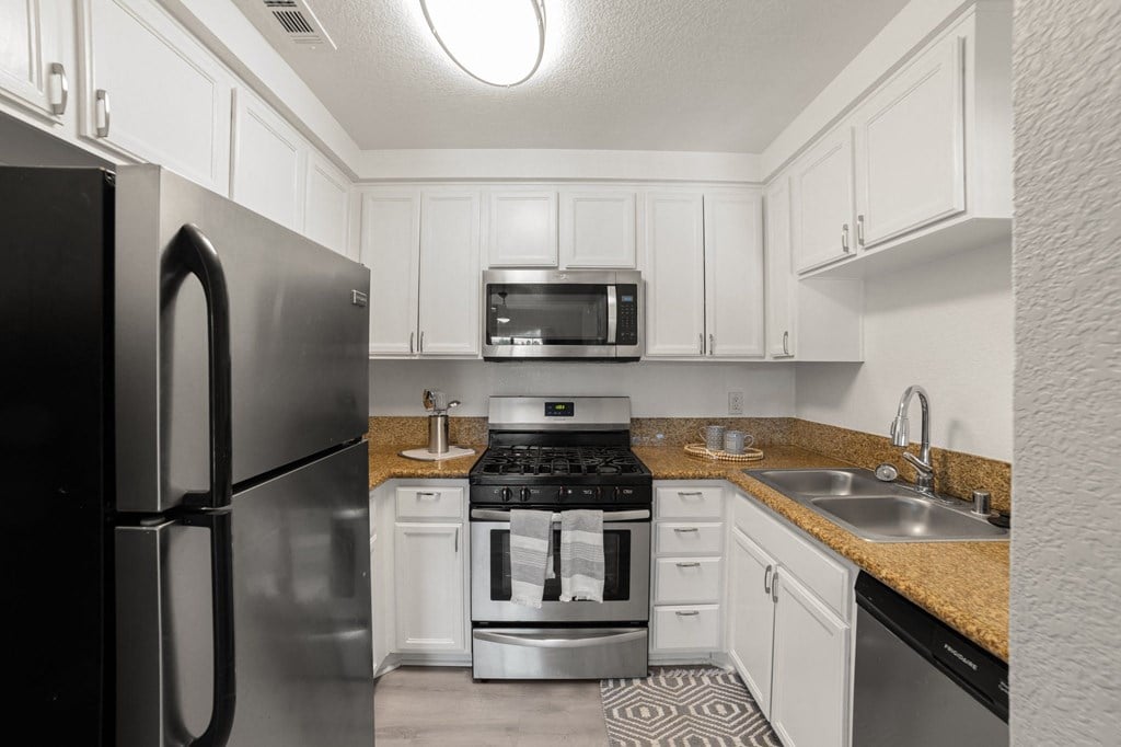A black refrigerator is in a kitchen with white cabinets.