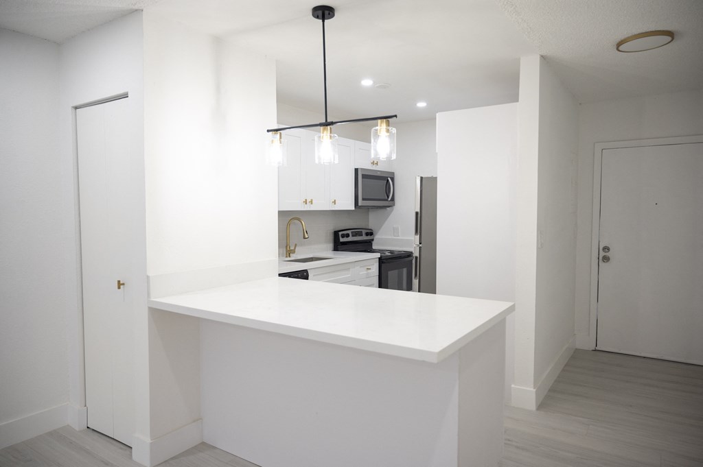 an empty kitchen with a white counter top and a refrigerator