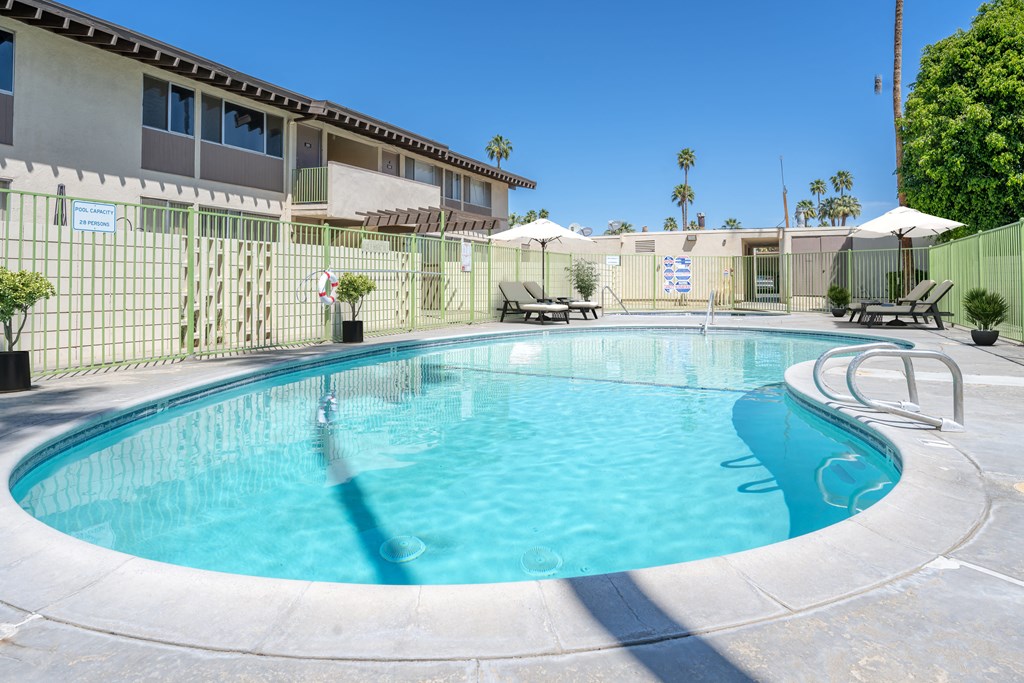A swimming pool surrounded by a fence and lounge chairs.