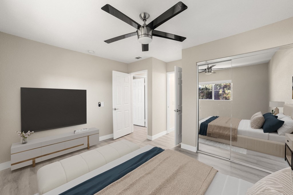 A modern bedroom with a large bed, a flat screen TV, and a ceiling fan.
