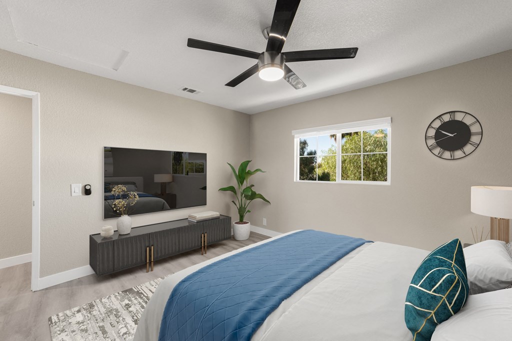 A bedroom with a bed, a ceiling fan, a mirror, a potted plant, and a clock on the wall.