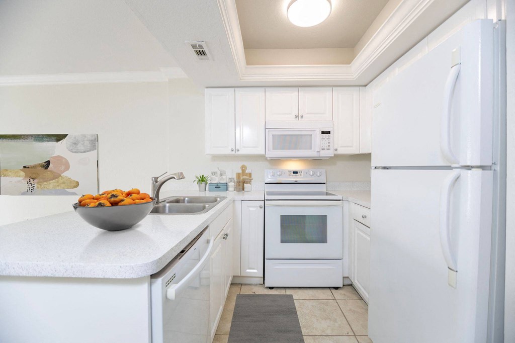 a small kitchen with white cabinets and a bowl of fruit on the counter