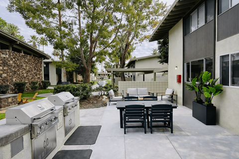 A patio with a table and chairs is surrounded by a stone wall and trees.