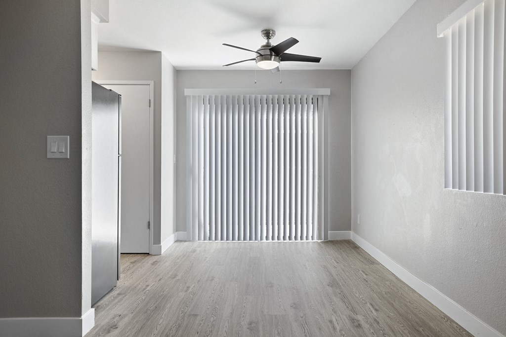 A room with a ceiling fan and a window with vertical blinds.