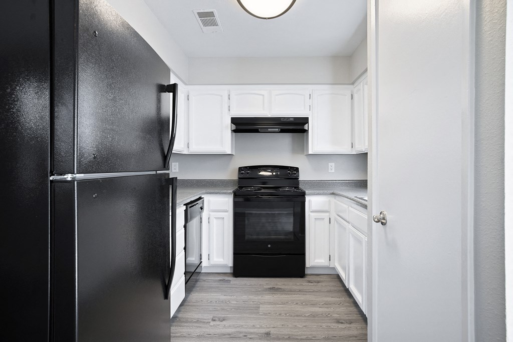 A black refrigerator stands in a kitchen with white cabinets and a black stove.