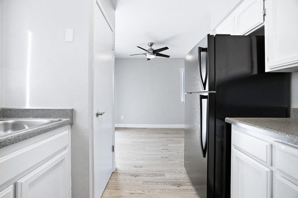 A black refrigerator in a kitchen with white cabinets.