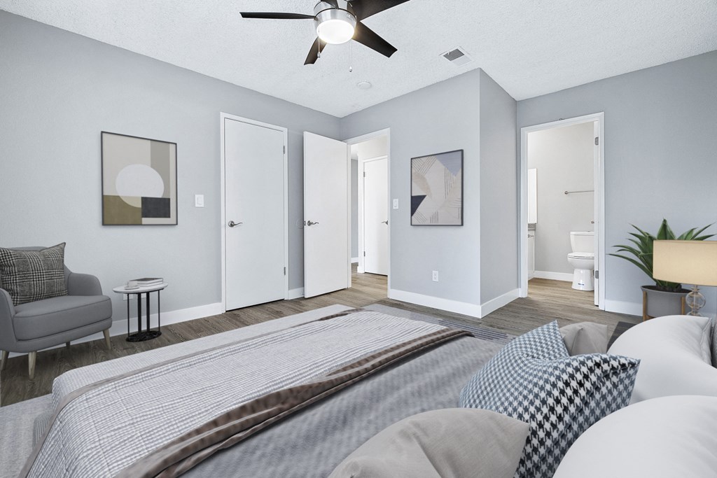 A bedroom with a bed, a couch, a chair, a potted plant, and a ceiling fan.