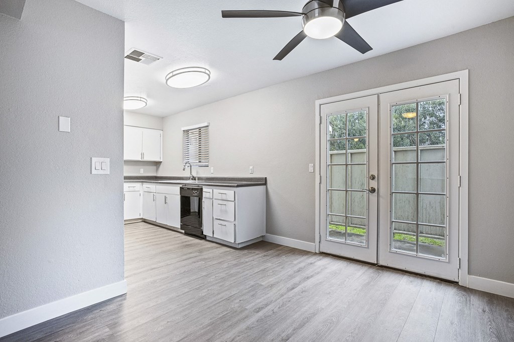 an empty living room and kitchen with a ceiling fan and glass doors