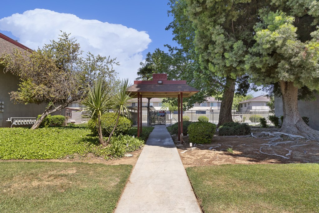 a sidewalk leading to a gazebo in a yard with trees