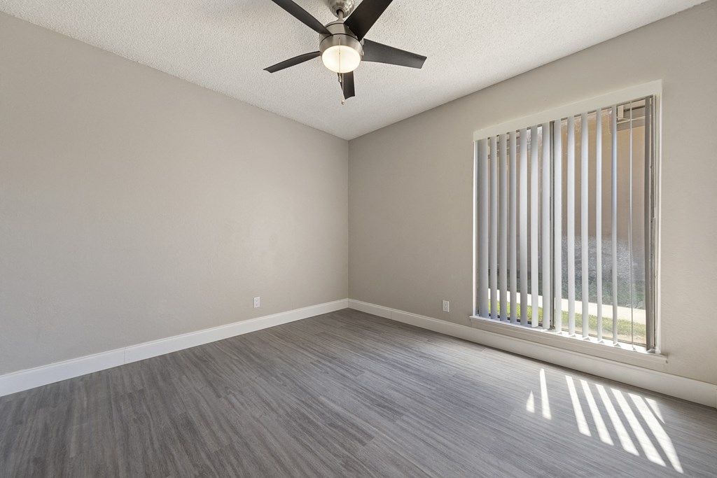 an empty living room with a large window and a ceiling fan