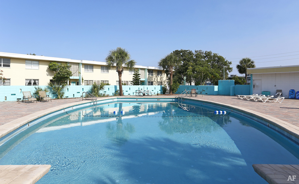 a resort style swimming pool with chaise lounge chairs and palm trees in the background