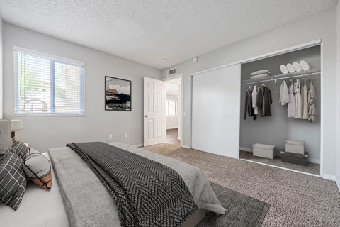 A bedroom with a large bed and a closet with clothes hanging.