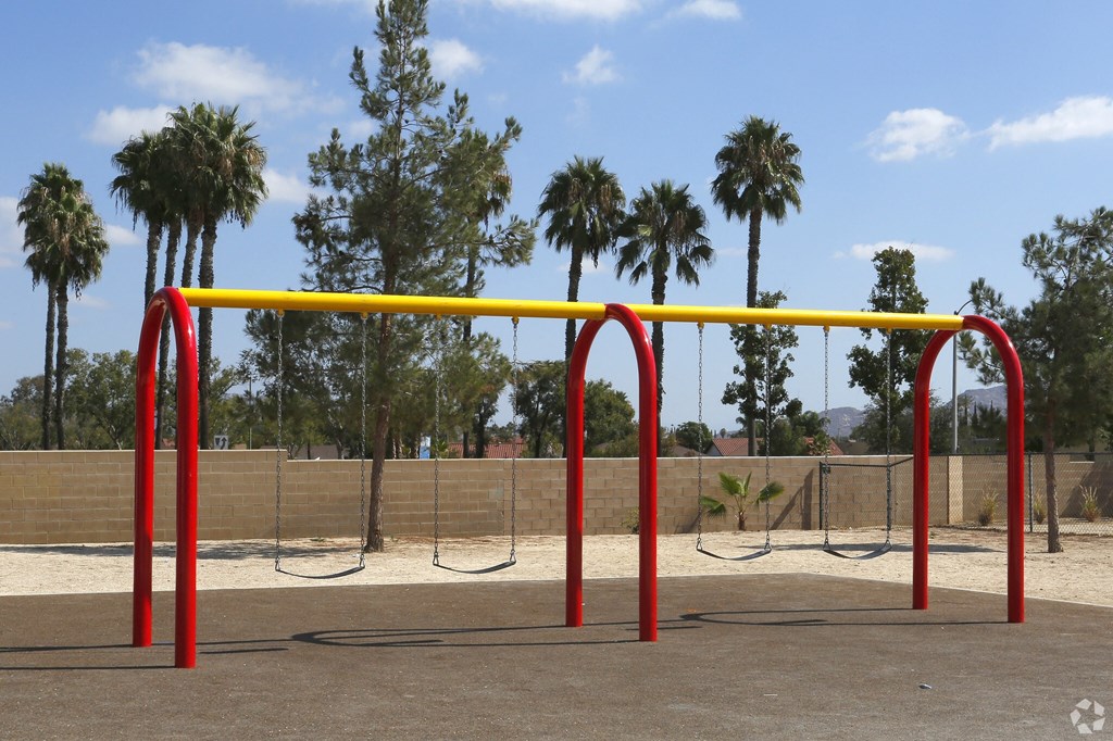 A playground with a red and yellow swing set.