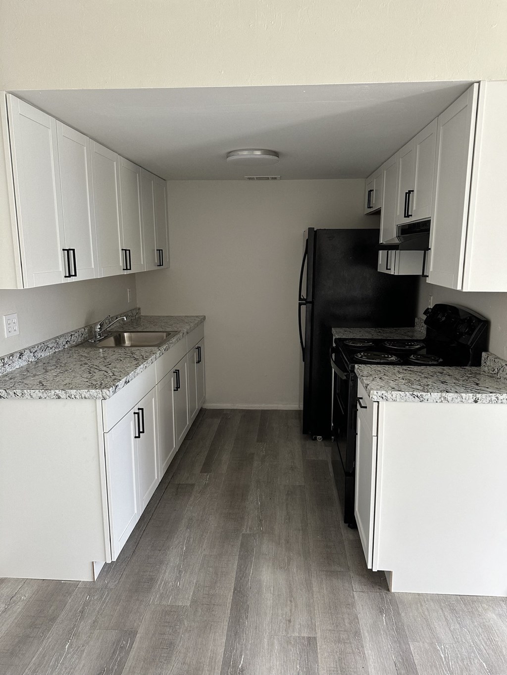 an empty kitchen with white cabinets and a black refrigerator