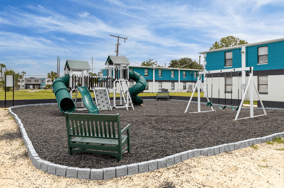 a playground with a slide and swings and a bench in front of a building