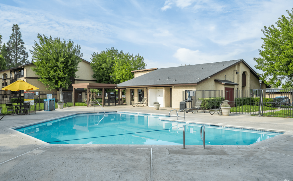 A large swimming pool in front of a building with a yellow umbrella and a black fence.