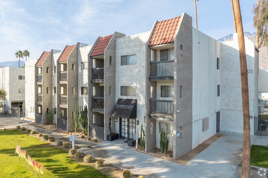 A row of modern buildings with balconies and a green lawn in front.