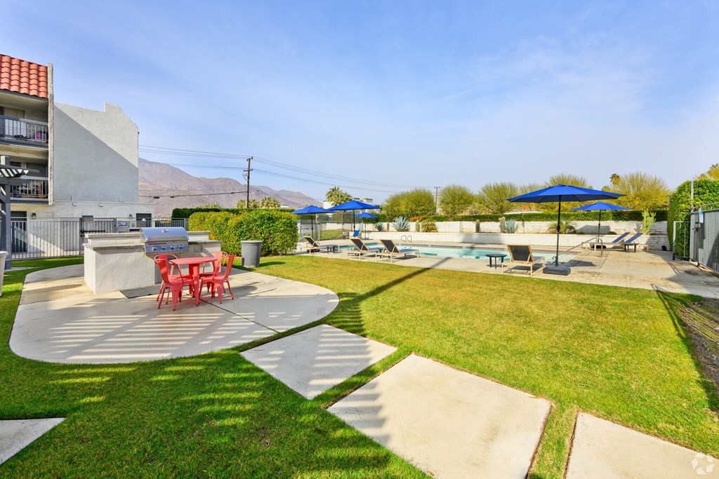 A sunny day at a poolside with a red table and chairs.