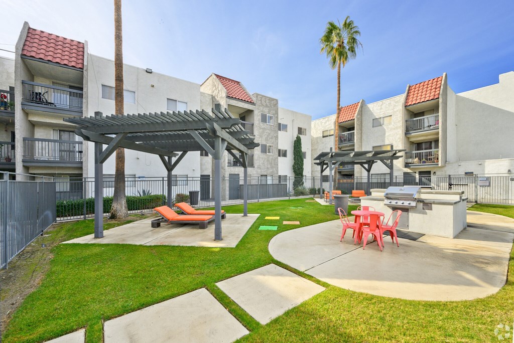 A sunny day at a courtyard with a palm tree, a picnic table, and a shaded area.