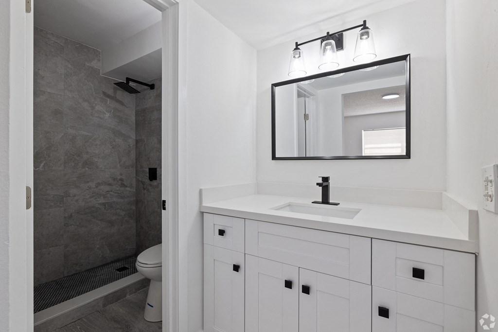 a bathroom with white cabinets and a gray shower