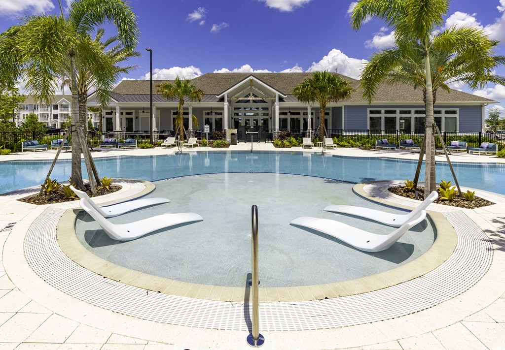 a large swimming pool with white chairs and a building in the background